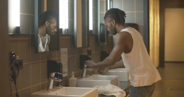 Vue latérale du jeune Afro-Américain s'approchant pour couler et laver le visage. Portrait de touriste détendu en utilisant salle de bains dans l'auberge. Tatoué gars confiant dans la matinée à l'hôtel. — Video