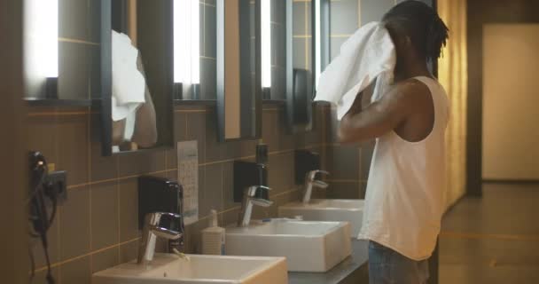 Vista laterale dell'uomo afroamericano sicuro di sé che pulisce il viso con un asciugamano bianco. Ritratto di giovane tatuato che lascia il bagno al mattino. Turismo maschile in hotel o ostello. — Video Stock