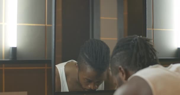 Riflessione di fiducioso giovane afroamericano viso lavaggio al mattino. Ritratto ravvicinato di bel ragazzo in bagno a casa. Igiene e routine. — Video Stock