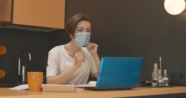 Covid maskeli genç bir kadın internette konuşuyor. Coronavirus virüsü salgını sırasında evde kalan güzel esmer beyaz kadın portresi. Covid-19 virüsü. — Stok video
