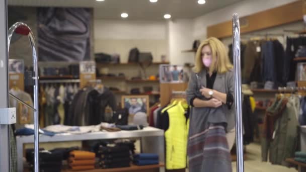 Nerviosa mujer caucásica en coronavirus mascarilla caminando a la salida de la tienda con ropa robada y huyendo. retrato de una ladrona robando bienes en un centro comercial durante la pandemia viral de Covid-19. — Vídeo de stock