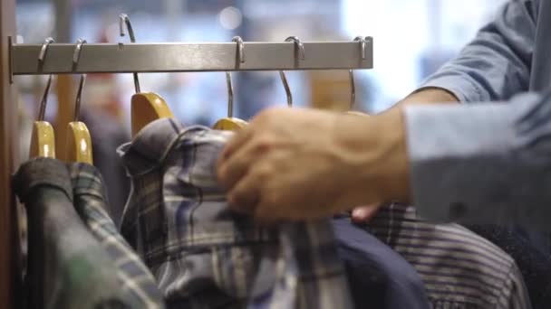 Blanke mannenhanden die overhemden aan hangers in de winkel aanraken. Onherkenbare man die kleding kiest in een winkelcentrum of winkel. Een mannelijke klant die kleding selecteert. Modeconcept. — Stockvideo