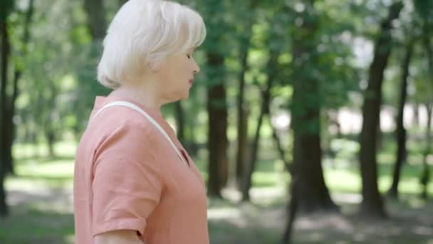 Pohled na důchodce, jak se zastavuje ve slunečném parku kvůli bolesti na hrudi. Kamera se blíží k bělošské ženě, která má venku příznaky infarktu. Zdravotní péče a stárnutí koncepce. — Stock video