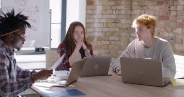 Üç şaşkın iş arkadaşı ofiste girişimi tartışıyor. İçerde çok ırklı takım planlama projesinin portresi. Genç erkekler ve kadınlar konuşuyor ve el kol hareketi yapıyorlar. Sinema 4k ProRes Merkezi.