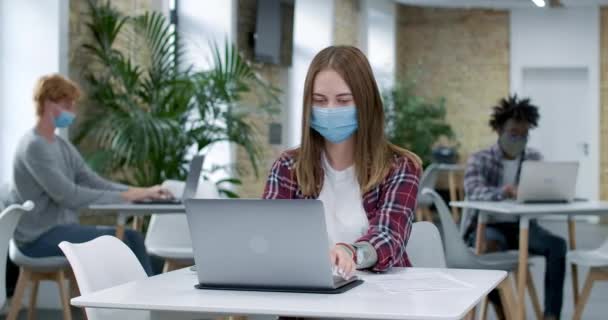 Covid-19 'daki beyaz kadın, arka planda çalışan çok ırklı iş arkadaşlarıyla çevrimiçi olarak maske takıyor. Koronavirüs salgını sırasında iş. Sinema 4k Karargahı. — Stok video