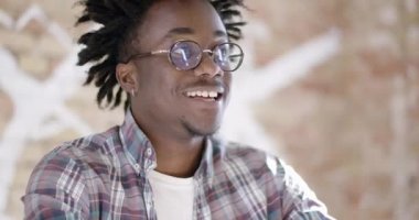 Gözlüklü, gülümseyen Afro-Amerikan genç adamın yakın çekimi. Baş parmağını kaldırıyor ve güneşli ofiste el çırpıyor. Erkek yatırımcı girişimi onaylıyor. Sinema 4k ProRes Merkezi.