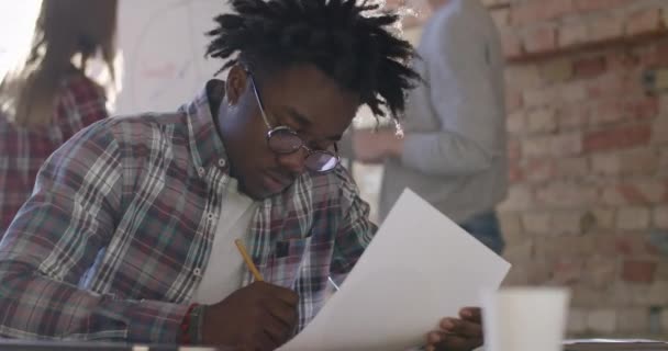 Portret van een nerveuze jonge Afro-Amerikaanse man die potlood breekt met wazige collega 's die op de achtergrond lopen. Mislukt gestresste mannelijke werknemer in functie. Cinema 4k ProRes Hoofdkwartier. — Stockvideo