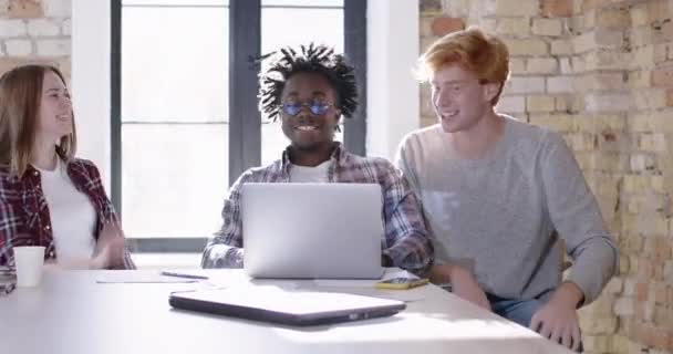 Tres compañeros de trabajo felices mostrando gesto de victoria y dando chocar los cinco en la oficina soleada. Retrato de alegres colegas jóvenes multiétnicos milenarios que se regocijan por el éxito de la startup. Sede del cine 4k ProRes. — Vídeos de Stock