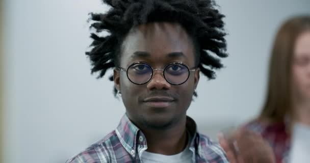 Close-up ansigt af glad afrikansk amerikansk mand i briller ser på kamera og smilende. Portræt af munter selvsikker smuk fyr poserer indendørs. Biograf 4k ProRes hovedkvarter. – Stock-video