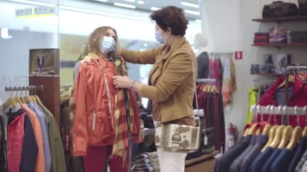 어머니와 딸은 코로나 바이러스가 유행하는 블랙 금요일에 상점에서 쇼핑을 하고 있다. 코비 디 우스 -19 마스크를 입은 백인 여성의 초상화. 구매 개념. — 비디오