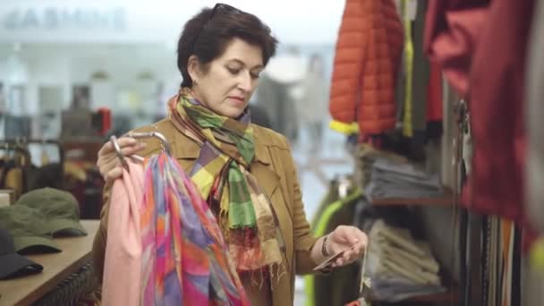 Portrait d'une élégante femme adulte qui choisit des écharpes dans un magasin de vêtements. Femme caucasienne confiante achetant tenue à la mode pendant les ventes Black Friday. Concept de style de vie et de consumérisme. — Video