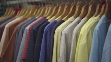 Bir sürü renkli erkek tişörtü giyim mağazasında askıda asılı. Alışveriş merkezinde elbise askıda..
