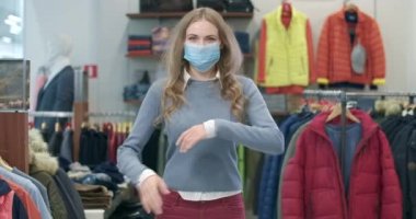 Covid-19 yüz maskeli güzel bir kadın el ele tutuşup kameraya bakıyor. Coronavirus Kara Cuma günü giysi mağazasında poz veren kendine güvenen beyaz alışverişçinin portresi. Sinema 4k ProRes Merkezi.