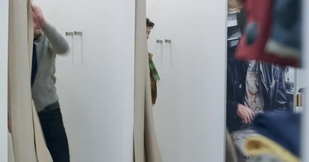 Hombre y mujer caucásicos confiados abriendo cortinas en el vestidor de la tienda de ropa y posando en prendas nuevas. Feliz pareja rica probándose ropa en las ventas del Viernes Negro. Sede del cine 4k ProRes. — Vídeo de stock