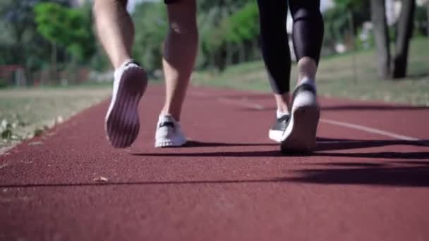 Legs of Caucasian sportsman and sportswoman walking along running track on sunny summer day. Unrecognizable man and woman strolling after workout outdoors. Sport and healthy lifestyle. — Stock Video