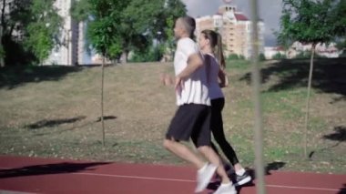 Şehir koşu pistinde koşan sporcu ve sporcu kadının yan görüntüsü. Güneşli bir yaz gününde, gülümseyen adam ve kadının açık havada koşuşunun geniş bir görüntüsü. Spor ve yaşam tarzı kavramı.