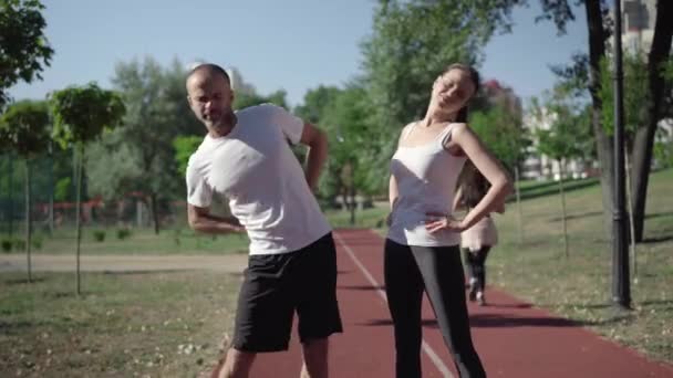 フィット感の肖像白人の大人のカップルは、ウォーミングアップ運動を終了し、スポーツ分野で逃げます.スポーツマンと女性ジョギング屋外で晴れた夏の朝に. — ストック動画
