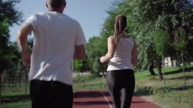 Neşeli güzel bir kadın açık havada daha hızlı koşması için erkeği cesaretlendiriyor. Neşeli Kafkas sporcusu sporcuyu geçiyor ve gülümsüyor. Yetişkin arkadaşlar güneşli yaz gününde antrenman yapıyor..