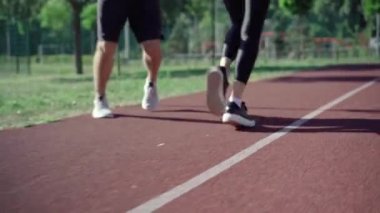 Açık havada güneşli pistte koşan tanınmayan fit erkek ve kadın bacakları. Spor ayakkabılı beyaz bir çift yaz sabahı koşuyor. Spor ve yaşam tarzı konsepti.