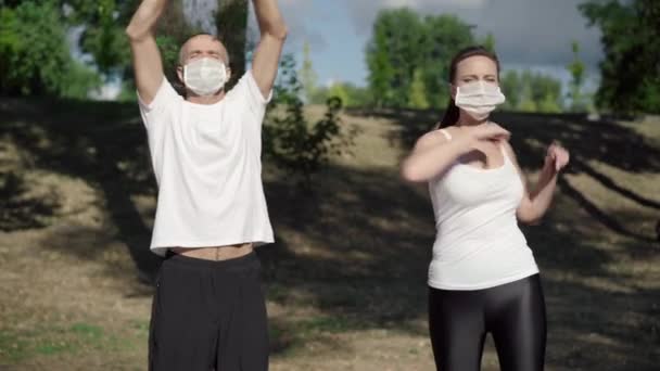 Pewny siebie biały mężczyzna i kobieta rozciągający się przed treningiem na świeżym powietrzu. Portret sportowców w maskach Covid-19 rozgrzewających się w słoneczny letni dzień. Koncepcja treningu koronawirusowego. — Wideo stockowe