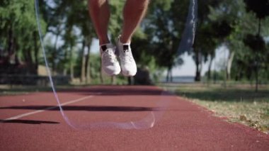 Açık havada koşu pistinde ip atlayan tanınmamış beyaz sporcu. Güneşli yaz gününde formda bir sporcunun kardiyo ısınma egzersizi. Spor ve sağlıklı yaşam tarzı..