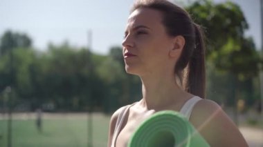 Güneş ışığının altında duran ve şişeden su içen güzel Kafkas sporcu kadının yan görüntüsü. Esmer, kendine güvenen bir kadın boğuluyor ve öne eğiliyor..
