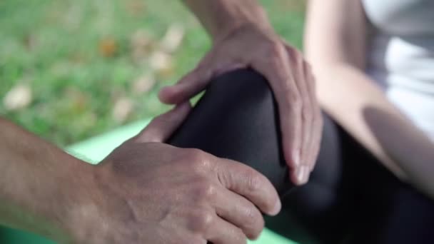 Close-up van mannelijke blanke handen masseren vrouwelijke knie in zwarte leggings. Onherkenbare man palpeert gewond been van sportvrouw in het zonlicht buiten. Begrip sportblessure. — Stockvideo