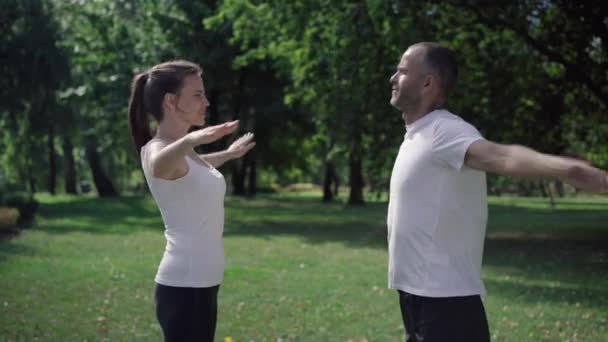 Side view of sportswoman training with personal coach outdoors on sunny summer day. Confident trainer showing warmup exercise and talking, woman repeating after man. Sport and workout. — Wideo stockowe