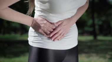 Tanımlanamayan zayıf, beyaz bir kadının dışarıda mide ağrısı var. Genç atletik bayan elleriyle karnını tutuyor. Sağlık sorunları ve apandisit iltihabı belirtileri.