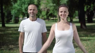 Spor giyim sektöründe güçlü bir jest ve kameraya gülümseyen kadın ve erkek pozitiftir. Güzel sporcu kadın ve dışarıda antremandan sonra poz veren yakışıklı yetişkin adam. Eğitim ve spor konsepti.