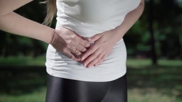 Unrecognizable slim Caucasian woman having stomach pain outdoors. Young athletic lady holding belly with hands. Health care problems and symptoms of appendicitis inflammation. — Stock Video