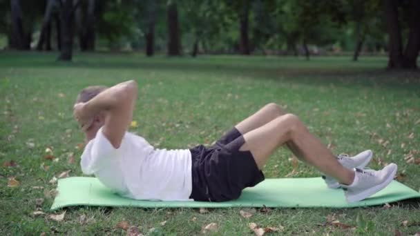 Amplo tiro de caber esportista caucasiano bombeamento imprensa no tapete de exercício ao ar livre. Exercício matutino de homem caucasiano atlético confiante no prado de verão verde. — Vídeo de Stock