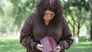 Yaşlı emeklinin boş cüzdanı açması ve kafasını sallayarak göğsüne yaklaşması. Güneşli şehir parkında parasız duran zavallı beyaz kadının portresi. Yoksulluk kavramı.