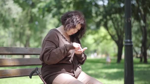 Camera approaches to sad senior woman counting coins on bench in city park. Portrait of unhappy Caucasian female retiree shaking head on sunny summer day. Poorness and inequality concept. — Stock Video