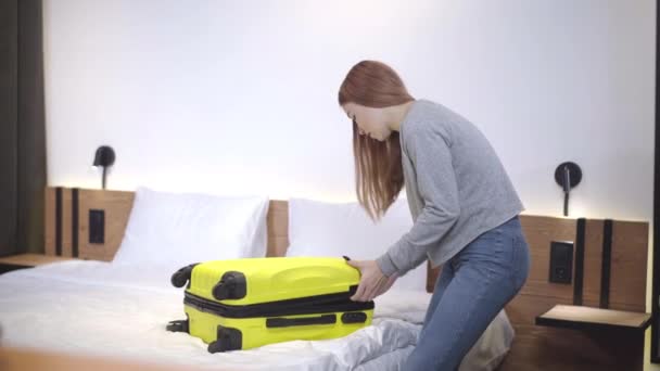 Mooi tienermeisje dat de gele reistas sluit. Portret van een zelfverzekerde blanke tiener die spullen inpakt voordat hij naar de slaapkamer gaat. Toerisme en reizen. — Stockvideo