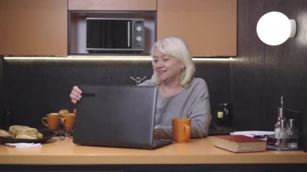 Femme âgée insouciante ouvrant un ordinateur portable et portant des lunettes. portrait d'un magnifique retraité caucasien détendu surfant sur Internet dans la cuisine le matin. Concept de loisirs et de style de vie. — Video