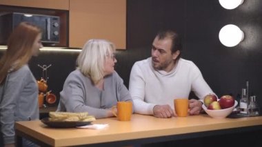 Neşeli genç kız mutfağa giriyor ve ailelere sarılıp çay içiyor. Kameraya bakıp gülümseyen mutlu bir beyaz aile. birlik ve iyi ilişki.