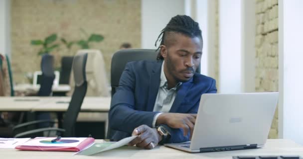 Retrato de um jovem empresário afro-americano bem-sucedido olhando para o laptop e fazendo um gesto de vitória. Feliz homem confiante torcendo o sucesso do projeto de startup online. Cinema 4k ProRes HQ. — Vídeo de Stock