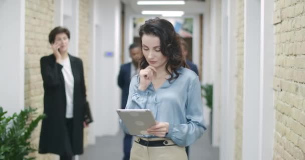 자신감 있고 생각깊은 백인 여성이 사무실에서 태블릿을 사용하고 여러 민족의 동료나 직원에게 인사를 한다. 성공 한 여성 CEO 계획 워크 플로우. 시네마 4k ProRes HQ. — 비디오