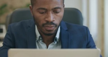 Laptop klavyesinde yazan ve düşünen odaklanmış sakallı Afrikalı Amerikalı adamın yakın çekimi. Ofiste çalışan kendine güvenen genç ve yakışıklı iş adamının portresi. Sinema 4k ProRes Merkezi.