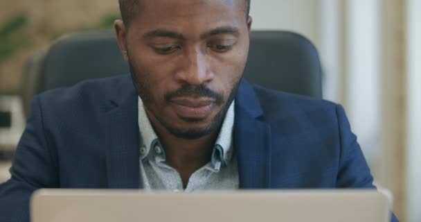 Közelkép a fókuszált szakállas afro-amerikai férfiról, aki gépel a laptop billentyűzetén és gondolkodik. Portré magabiztos fiatal jóképű üzletemberről, aki online dolgozik az irodában. Cinema 4k ProRes főhadiszállás. — Stock videók