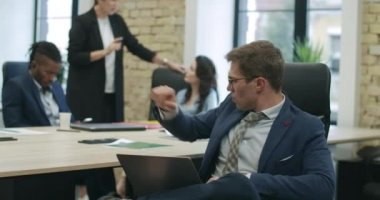 Gözlüklü yakışıklı, kendine güvenen beyaz adam arka planda konuşan bulanık meslektaşlarıyla başlangıç analizi yapıyor. Başarılı genç iş adamı kameraya bakıyor. Sinema 4k ProRes Merkezi.