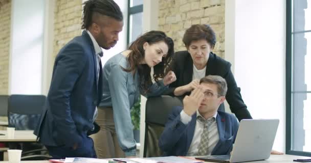 Een zelfverzekerde man in een bril die opstarten uitlegt aan multi-etnische collega 's in het kantoor. Jonge knappe blanke zakenman met een idee aan collega 's. Cinema 4k ProRes Hoofdkwartier. — Stockvideo