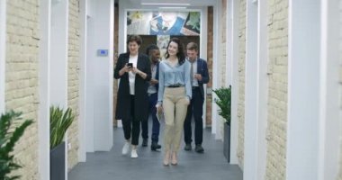 Ofis koridorunda yürüyen ve konuşan dört pozitif çok ırklı iş arkadaşı. Başarılı iş toplantısından ve sohbetten sonra dönen mutlu meslektaşlar. Takım çalışması başarılı. Sinema 4k ProRes Merkezi.