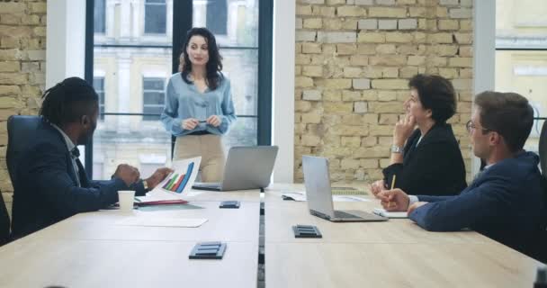 Ofisteki iş toplantısını yöneten kendine güvenen güzel genç CEO. Gülümseyen beyaz bir kadının portresi. İçerideki çalışanlarla yeni başlayanları tartışıyor. Sinema 4k ProRes Merkezi. — Stok video