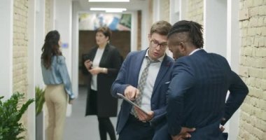 Başarılı Afro-Amerikalı ve Kafkas işadamları internette tablet üzerinde sörf yapıyor ve ofis koridorunda el sıkışıyorlar. Kendine güvenen çoklu etnik ortaklar anlaşma yapıyor. Sinema 4k ProRes Merkezi.