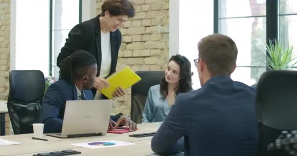 Quatre collègues multiethniques joyeux bavardant au bureau. Des hommes et des femmes caucasiens et afro-américains souriants qui parlent à l'intérieur. Coopération et travail d'équipe. Siège social Cinema 4k ProRes. — Video