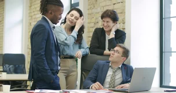 Colegas multiétnicos discutindo projeto com jovem sentado à mesa com laptop. Colegas caucasianos e afro-americanos bem sucedidos analisando startup de negócios no escritório. Cinema 4k ProRes HQ — Vídeo de Stock