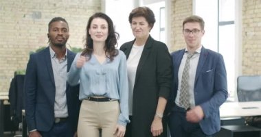Bir grup çok ırklı iş arkadaşı ofiste poz veriyor. Kendinden emin Afro-Amerikan ve beyaz kadın kameraya bakıp gülümsüyor. İşbirliği ve iş. Sinema 4k ProRes Merkezi.