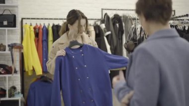 Elbise dükkanında arkadaşıyla kıyafet seçen beyaz bir kadın. Alışveriş merkezinde kıyafet seçen güzel bir müşterinin portresi. Yaşam tarzı ve arkadaşlık kavramı.